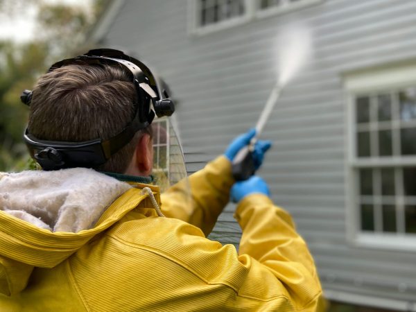 pexels photo 5652626 5652626 Person cleaning house siding with a pressure washer, wearing protective gear in a yellow raincoat.